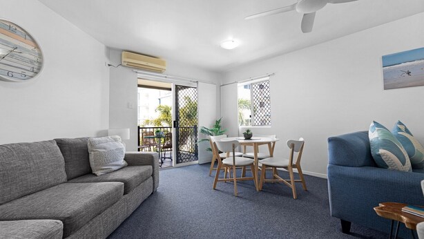 Ein modernes Wohnzimmer mit grauem Sofa, blauem Sessel, Esstisch mit Stühlen und Deckenventilator.