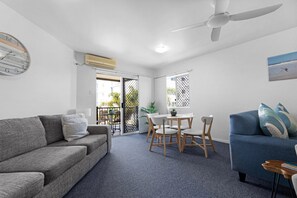 Una sala de estar moderna con un sofá gris, un sillón azul, una mesa de comedor con sillas y un ventilador de techo.
