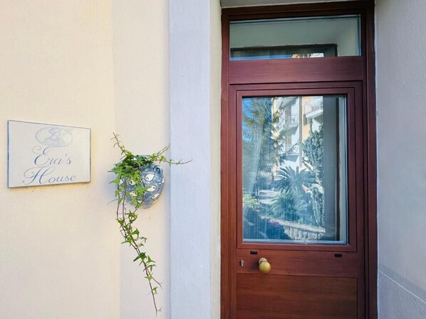 Eine Holztür mit Glasschiebeelement, ein Schild mit der Aufschrift 'Eve's House' und eine hängende Pflanze mit Ranken.