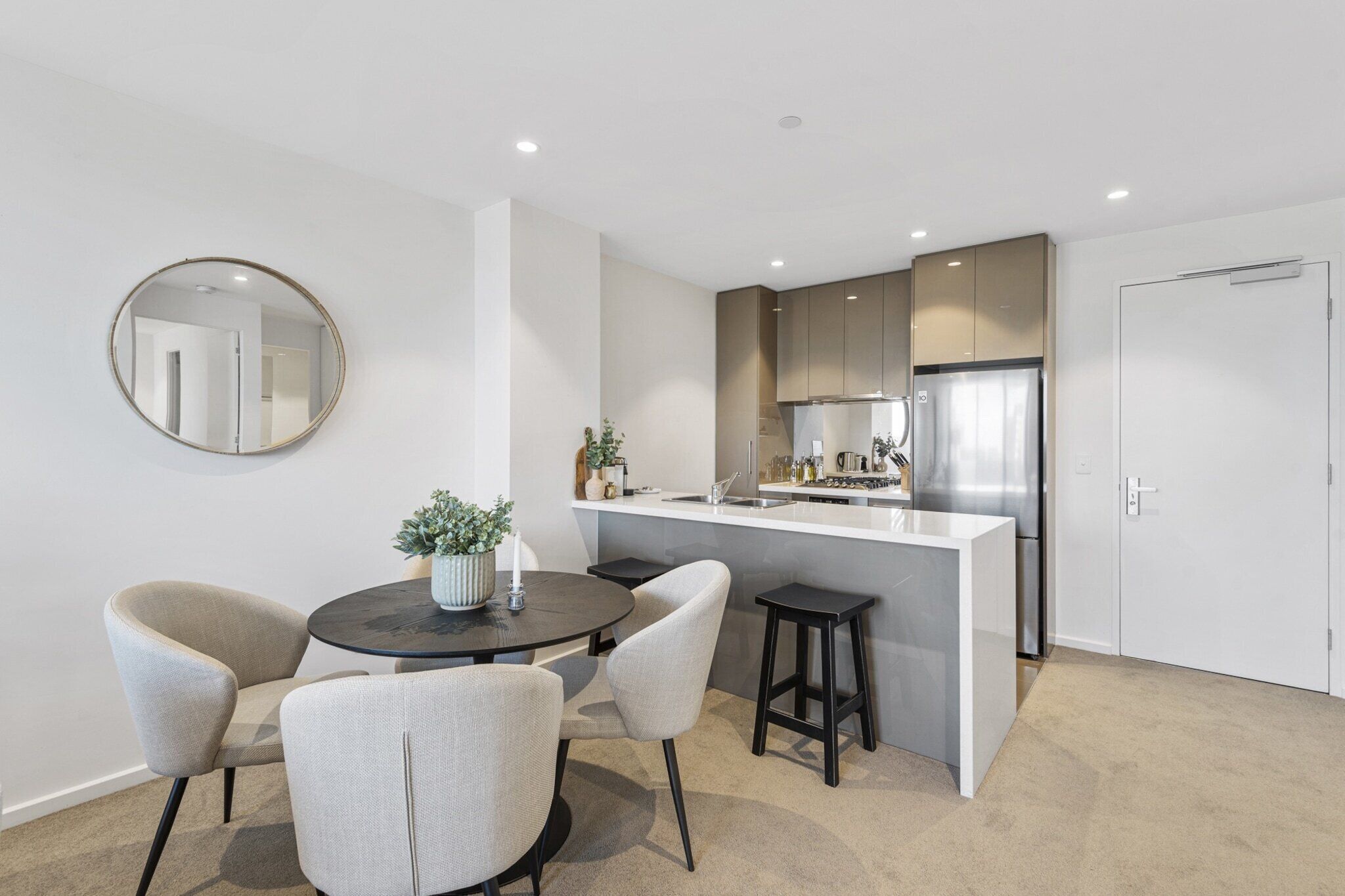 A modern kitchen with a central island, a dining area with chairs, a round table, and a mirror on the wall.