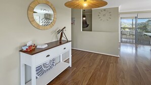 A modern interior with a wooden console table, a round mirror, a wall clock, and a hanging light fixture. - Coastal Upper-Level Home with Pool Access (Batehaven)
