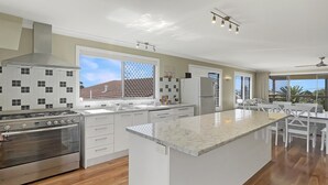 A modern kitchen with a large island, stainless steel appliances, and a view of the outdoors. - Coastal Upper-Level Home with Pool Access (Batehaven)