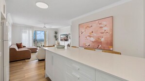 A modern kitchen with a white countertop, a large painting, and a view to the outside. - Bright 2-Bed Apartment with Stunning Ocean Views (Kings Beach)