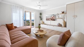 A modern living room with a large sofa, a coffee table, and a view of the sea through the glass door. - Bright 2-Bed Apartment with Stunning Ocean Views (Kings Beach)