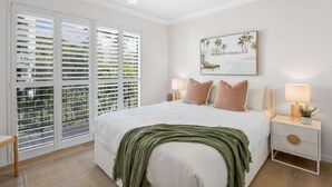 A bedroom with a large bed, a nightstand with a lamp, and a painting of a beach scene. - Bright 2-Bed Apartment with Stunning Ocean Views (Kings Beach)