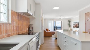 A modern kitchen with white cabinets, a large island, and a view to the living area. - Bright 2-Bed Apartment with Stunning Ocean Views (Kings Beach)