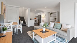 A modern apartment with a dining area, a living room with a sofa and coffee table, a kitchen, and a staircase leading to an upper floor. - Stylish 1-Bed Apartment with Balcony & Pool Access (Turner)