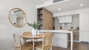 A modern kitchen with a central island, white cabinets, and a dining area with wicker chairs and a round table. - Trendy 1-Bed Retreat in Fremantle with Rooftop (North Fremantle)