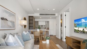 A modern living room with a sofa, coffee table, and TV. There is a kitchen area with cabinets and a dining table. - Trendy 1-Bed Retreat in Fremantle with Rooftop (North Fremantle)