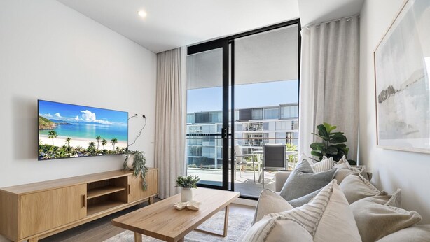 A modern living room with a wooden coffee table, a beige sofa, and a flat-screen TV mounted on the wall. - Trendy 1-Bed Retreat in Fremantle with Rooftop (North Fremantle)