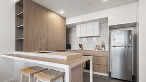 A modern kitchen with a central island, wooden cabinetry, a stainless steel refrigerator, and a built-in sink. - Modern 1-Bed Apartment with Views in Fremantle (North Fremantle)