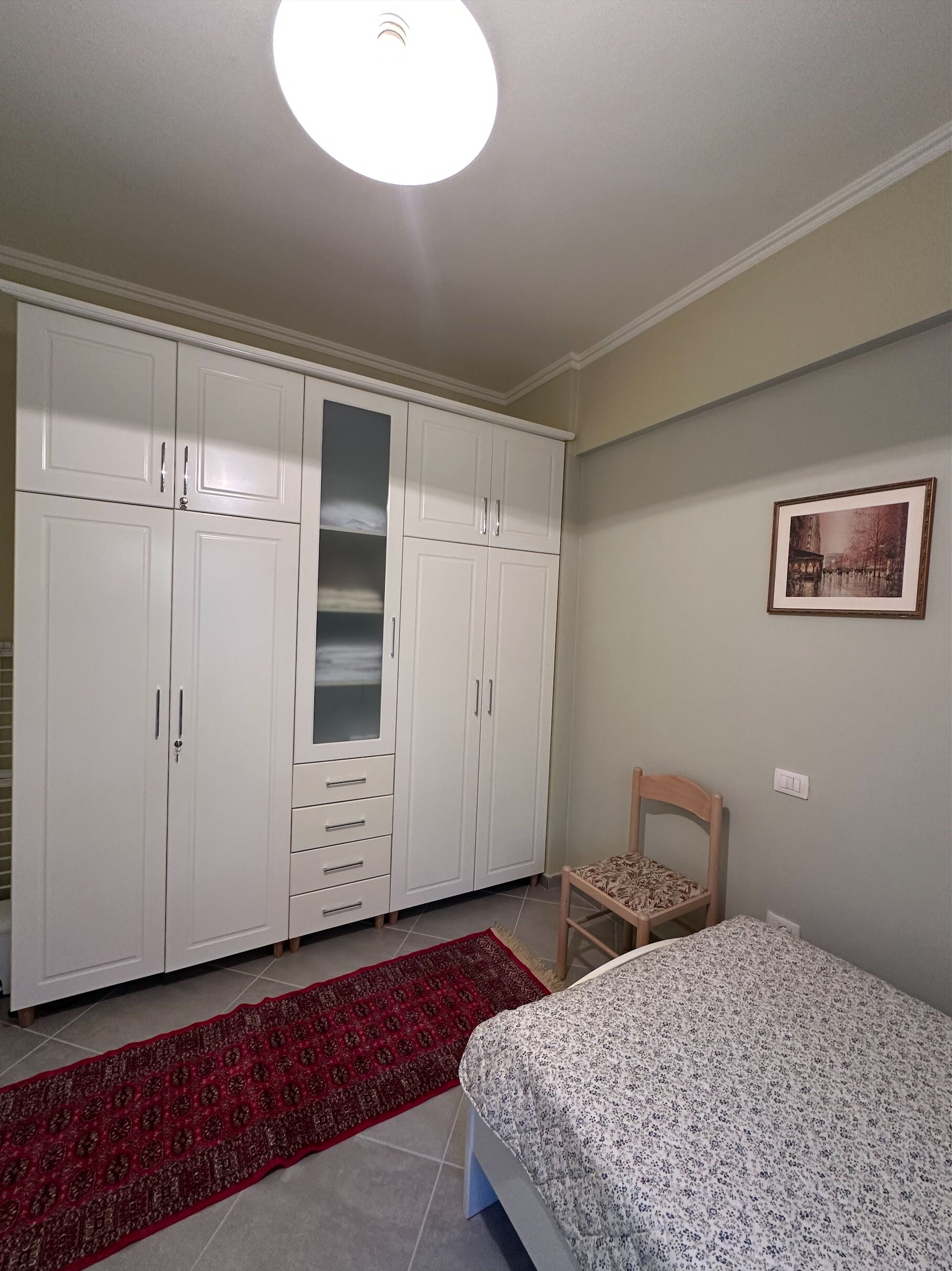 Een slaapkamer met een bed, een stoel, een kledingkast en een rood vloerkleed.