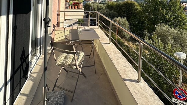 Un balcón con una mesa y sillas, un parasol grande y vistas a la ciudad y las montañas.