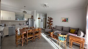Una cocina moderna con armarios blancos, una mesa de comedor con sillas y una sala de estar con sofá y mesa baja.