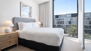 Ett modernt hotellrum med en stor säng, två sängbord med lampor, ett inramat konstverk på väggen och ett stort fönster med utsikt över stadsbilden.