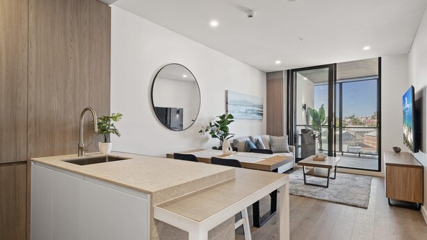 A modern kitchen with a large island, a dining area with a sofa and coffee table, and a living area with a TV and large windows. - Charming 1-Bed with Rooftop Access & Parking (North Fremantle)