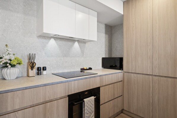 Una cocina moderna con horno empotrado, placa de inducción negra y muebles de madera.