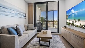 A modern living room with a sofa, coffee table, and a large painting of a beach scene. - Charming 1-Bed with Rooftop Access & Parking (North Fremantle)