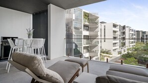 En moderne balkon med spiseplads, inklusive et bord og stole, samt udsigt til omkringliggende bygninger.