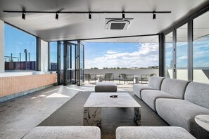 A modern outdoor seating area with a marble table, grey sofa, and chairs, overlooking a cityscape. - Stylish 2-Bed Unit with Views & Rooftop Access (North Fremantle)