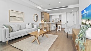 A modern living room with a sofa, coffee table, and dining area. - Stylish 2-Bed Unit with Views & Rooftop Access (North Fremantle)