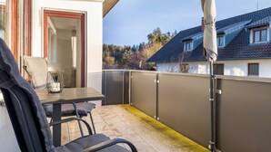 Un balcon avec une table et des chaises, une porte et une vue sur des maisons et des arbres.