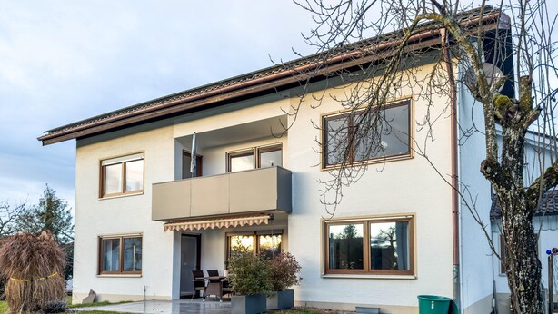 Une maison à deux étages dotée d’un balcon, d’une terrasse couverte et d’une pelouse bien entretenue.
