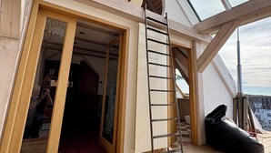 Tilava huone, jossa on korkea katto, puiset kattopalkit, kattovalokuvio ja suuri ikkuna.