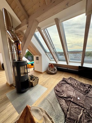 A cozy room with a wood-burning stove, a large window with a view of the water, and a comfortable seating area.