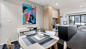Una cuina moderna amb una illa central, una zona de menjador amb taula i cadires blanques i una finestra gran que ofereix vista a l'exterior.