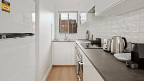 Una cocina moderna con armarios blancos, un refrigerador de acero inoxidable, un lavamanos y una cafetera.