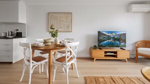 Una sala moderna con una mesa de comedor de madera, sillas de mimbre blanco, un televisor de pantalla plana y un aparador de madera.
