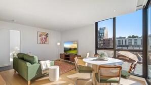 Un soggiorno moderno con un divano verde, un tavolo da pranzo con sedie, una TV e ampie finestre con vista sulla città.