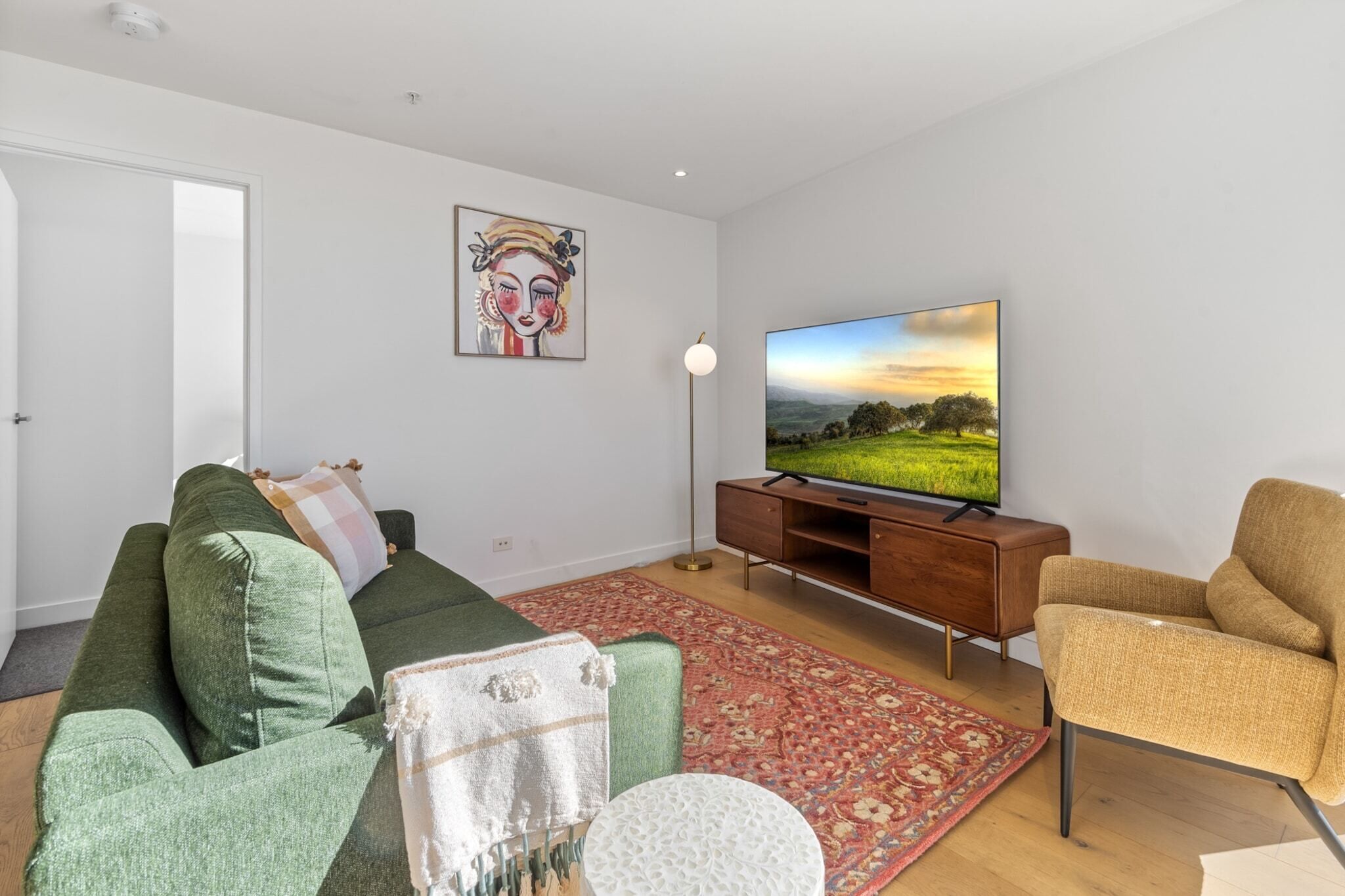 Ein Wohnzimmer mit einem grünen Sofa, einem beigen Sessel, einem Flachbildfernseher und einem roten Teppich mit Muster.