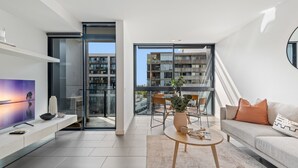 Un appartamento moderno con una televisione grande, un divano, un'area pranzo con sedie e vista su altri edifici.