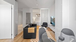 Un salon moderne avec un canapé, une table basse et un téléviseur. Une cloison en verre et une porte donnent accès à une autre pièce.