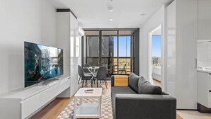 Un salon moderne doté d’un téléviseur à écran plat, d’un canapé gris, d’une table basse et d’un coin repas avec une table et des chaises en verre.
