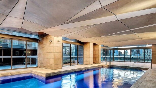 Une piscine intérieure moderne dotée d’un plafond au design géométrique, de grandes fenêtres et d’une vue sur le paysage urbain.