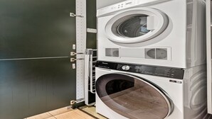 Una lavadora y secadora apiladas en una habitación con pared oscura y piso de baldosas.