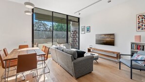 Una sala de estar moderna con una mesa de comedor de madera, un sofá gris y un amplio ventanal.