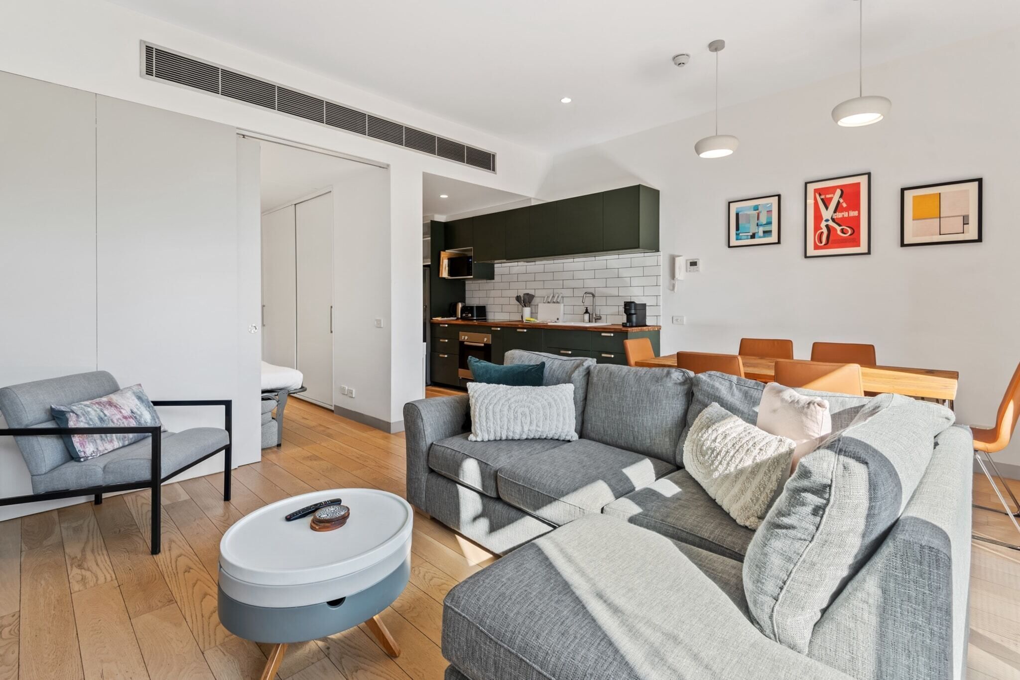 Un salon moderne avec un canapé gris, une petite table basse ronde et un coin repas comprenant une table et des chaises en bois.