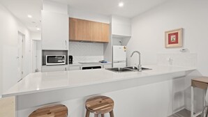 Une cuisine moderne avec des meubles blancs, un îlot central doté de tabourets, un four à micro-ondes, un réfrigérateur et un évier.