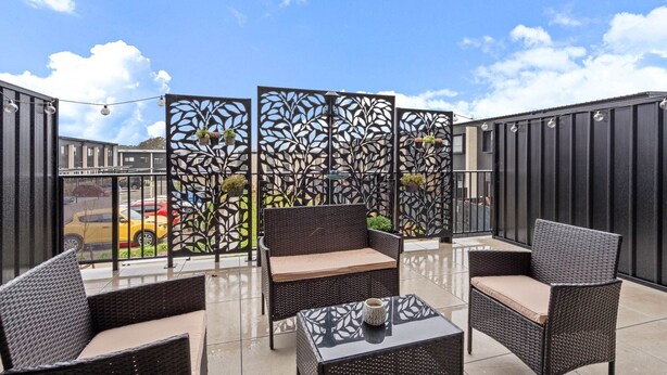 Une terrasse extérieure aménagée avec des meubles en osier, une table en verre et des panneaux décoratifs.
