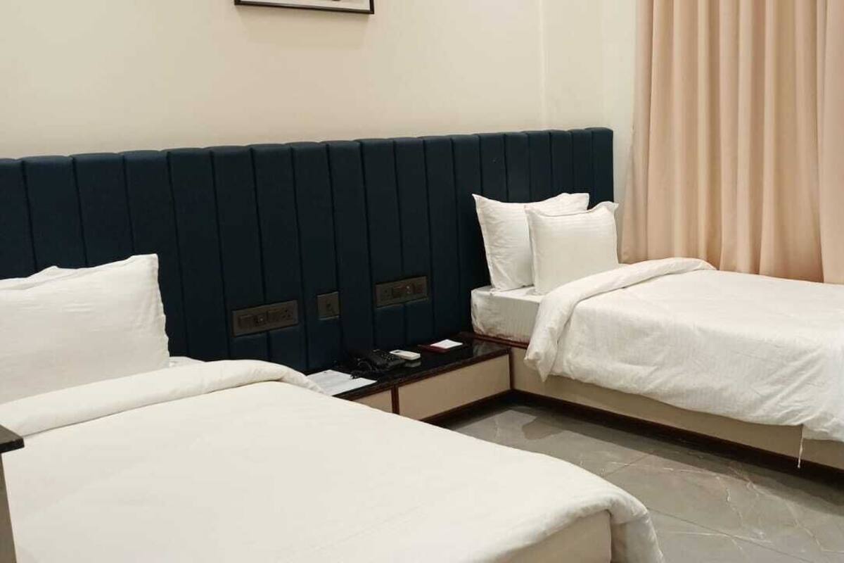 Una habitación de hotel con dos camas, una mesita de noche, una silla y una cortina.