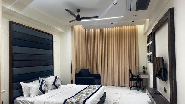 A modern bedroom with a large bed, a desk, a chair, and a television on the wall.