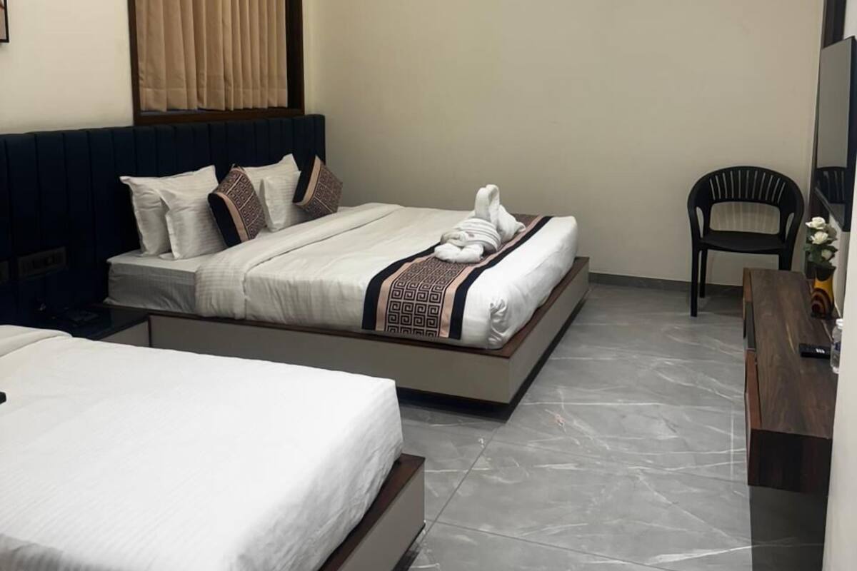 Habitación de hotel con dos camas, un escritorio, una silla y un ventanal grande con cortinas.