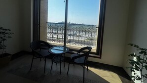 A balcony with a table and chairs, a potted plant, and a view of a beach and cityscape.