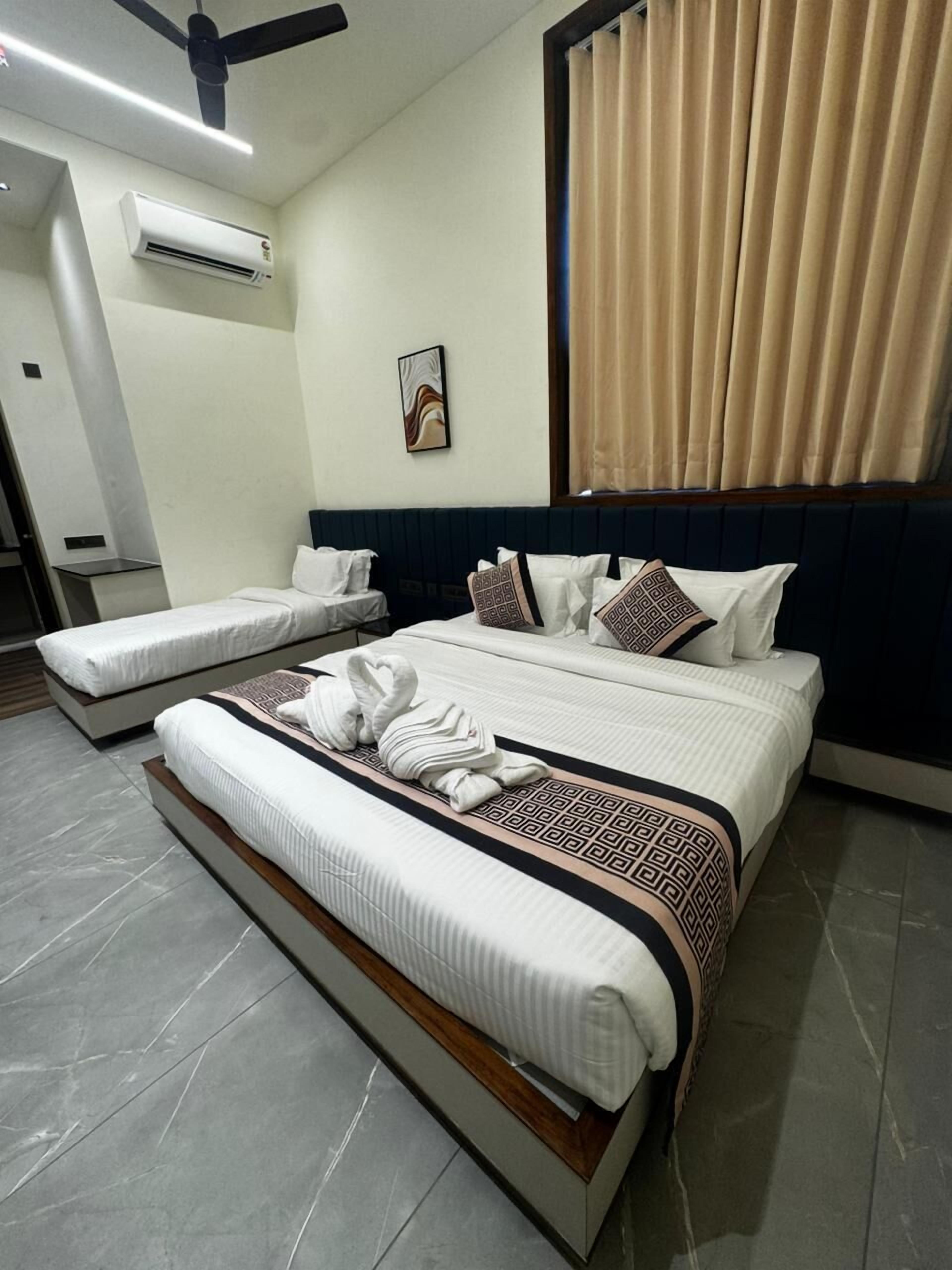 A hotel room with a large bed, a smaller bed, an air conditioning unit, a ceiling fan, a window with curtains, and a wall-mounted artwork.