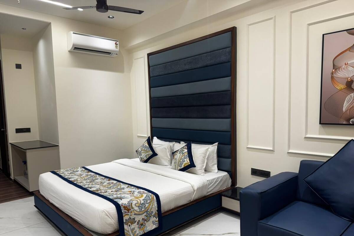 Un dormitorio moderno con una cama grande, un sillón tapizado en azul y un equipo de aire acondicionado en la pared.