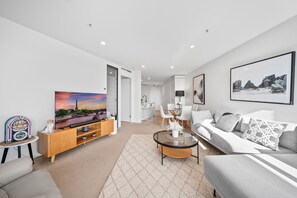 A modern living room with a flat-screen TV, a sofa, a coffee table, and a dining area with chairs.
